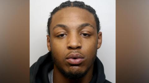 Dino Donaldson, a young man with a goatee beard, stares into a camera for a police custody photo.