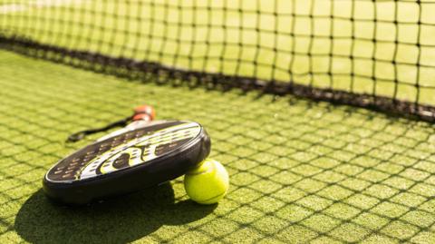 A padel racquet and balls on the floor next to a net