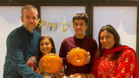 The  family wear traditional Hindu clothing while the two children hold pumpkins 