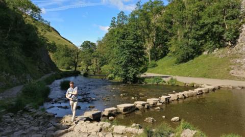 A young man walks across the stepping stones at Dovedale