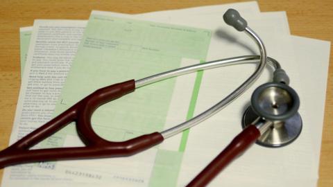 A stethoscope lies on a table on top of a blank prescription form.
