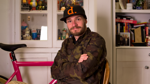 Gav Strange sat with his arms folded wearing a camo jacket and black cap. He is sat in front of white cabinets