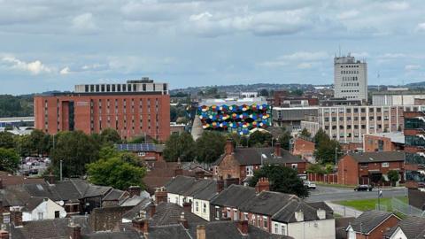 Elevated shot of the city-scape of Stoke-on-Trent, that features terraced homes in the foreground and a series of larger buildings further afield, including Hanley's One Smithfield building. 