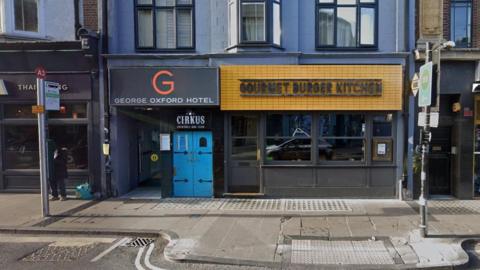 A Google street view image of a terraced building housing Gourmet Burger Kitchen on the ground floor. Next to it is the entrance to George Oxford Hotel. Inbetween are the double doors for Cirkus nightclub.