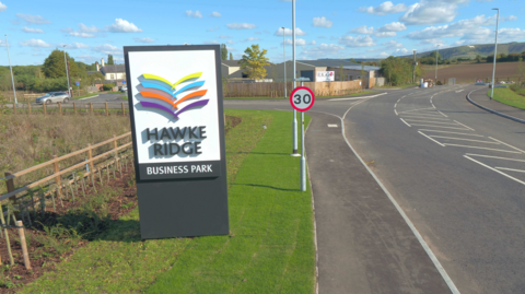 A road running past a sign which says 'Hawke Ridge business park'