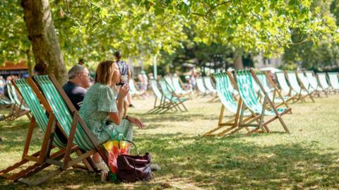 Two people sitting on deckchairs in a sunny park eating ice cream
