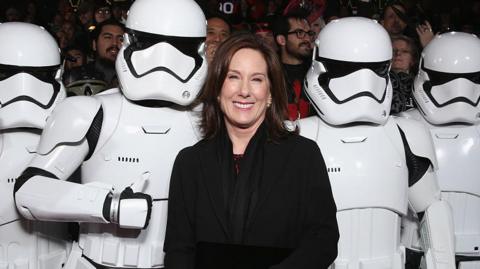Lucasfilm president Kathleen Kennedy in a black outfit poses for a photo beside four Star Wars Stormtroopers