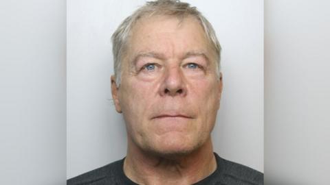 Headshot of a man with grey hair and blue eyes. He is wearing a black shirt. 