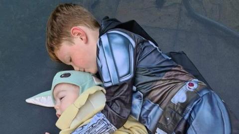 Harry cuddling his brother Reuben on a trampoline. Harry is kissing the back of his brother's head.