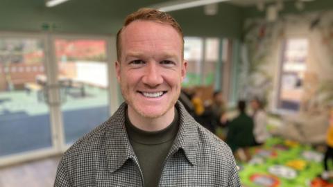 Greg Rutherford smiles at the camera, while standing inside the story room at the centre.