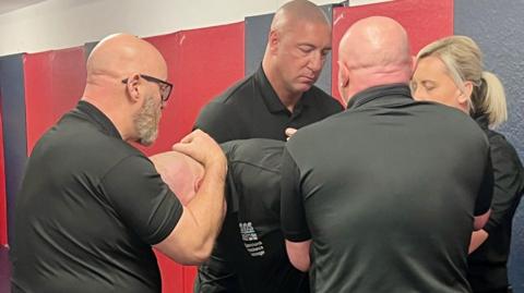 Four officers demonstrating the new restraint technique being introduced in Scottish jails.