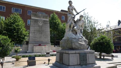The two memorials in Paragon Square, The Boer War one has a white stone sculpture of two soldiers while the cenotaph at the back of the square is a large stone obelisk with poppies laid beside it.