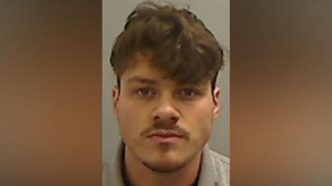 Mugshot of Walker. He has a moustache and faint goatee and thick brown hair, short at the sides and long over his forehead.