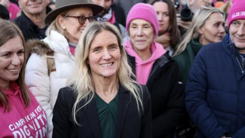 Kim Leadbeater stands with activists from Dignity in Dying campaign group after the bill was passed in Parliament Square in November. She is surrounded by activists, some wearing pink hats.