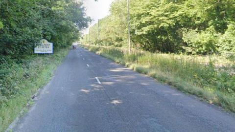 One side of the A413 dual carriageway with trees lining the edge of the road and a grass verge in the middle of the carriageway