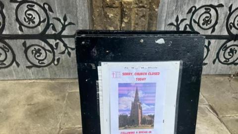 A sign in front of a large church door. It reads "Sorry, church closed". It is on a large blackboard.