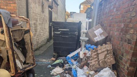 Rubbish dumped by a communal bin in an alleyway 