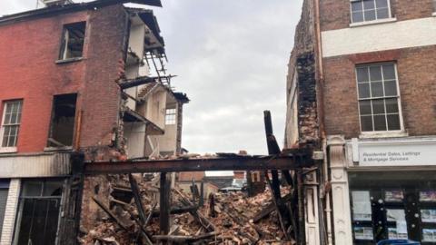 Fire-gutted building with debris spilling out onto a street of terraced building.