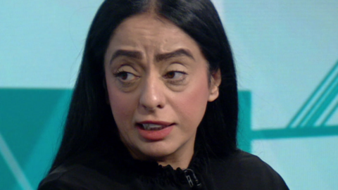 Arooj Shah, with shoulder-length dark hair and wearing a black top, speaks in a BBC TV studio.