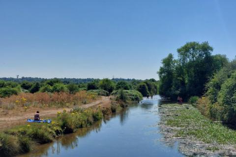 People relax and paddle along a calm river on a sunny day in Rickmansworth, Hertfordshire