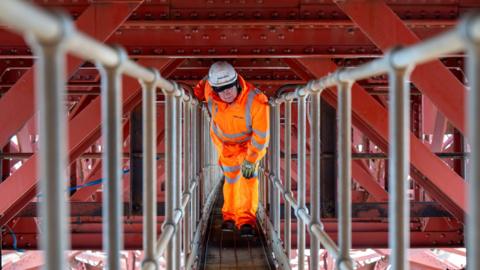 Man in orange hi-vis and white hard hat, underneath the railway line on the Forth Bridge