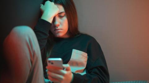 A morose looking teenager stares at a smartphone 