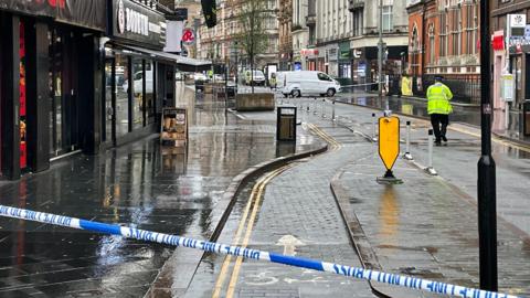 Police cordon tape across Granby Street in Leicester. A police officer stands at the scene.