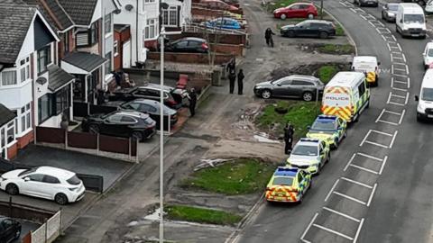 A drone image of police vehicles parked in Broad Avenue in Leicester and a number of officers around a property in the street 