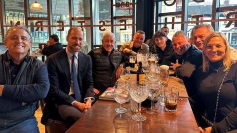 Prince William, second from the left, smiles alongside a group of Aston Villa fans around a table in Wetherspoon. Glasses of drinks are on the table