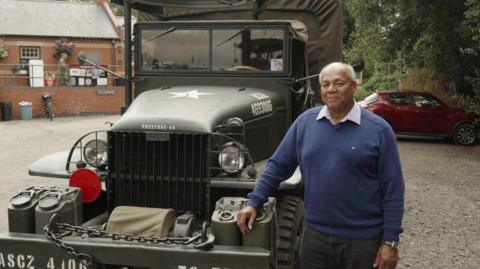 An elderly man stood next to a vintage military vehicle