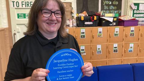 Jacqueline Hughes wearing a dark top and holding a blue plaque