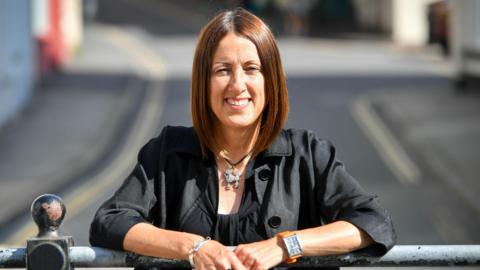 Jane Dodds stood leaning on a railing wearing a black jacket and top.