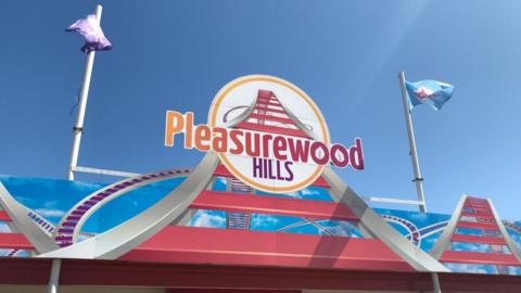 The main bright pink and blue sign reading Pleasurewood hills, flanked on both sides with flags