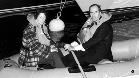 A black and white photo of two people rowing a boat.