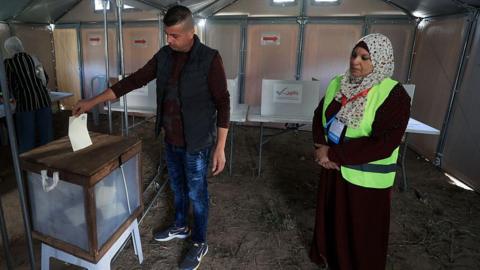 A man places a ballot into a box in a makeshift polling station in Gaza while a female election officials looks on