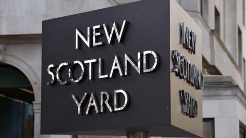 New Scotland Yard revolving sign. It is cube shaped and the lettering is in silver against a black background.