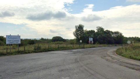 Entrance road leading to Augean at Port Clarence. There is a small white sign with the firm's name on it on the left-hand side of the road. The road is Tarmac and has a 30mph speed limit. It is surrounded by grassed areas and trees.