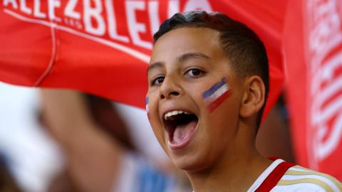 A boy with a painted face cheers while holding a flag