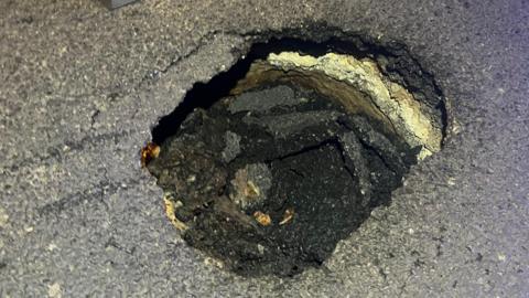 A tarmac road has partially collapsed. It is not possible to gauge the scale of the hole. 