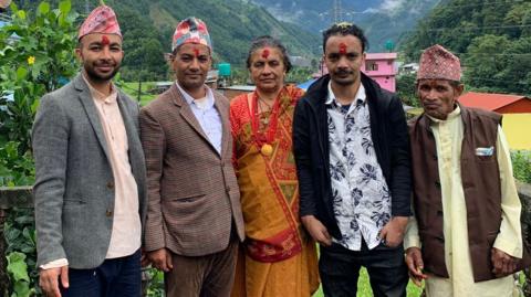 Four men and one woman side-by-side posing for a picture. There are green mountains behind them.