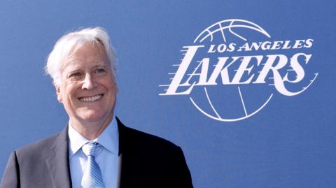 Mark Walter smiles in front of an LA Lakers sign