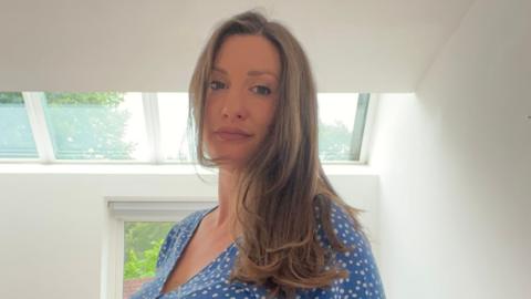 A woman with long light-brown hair wearing a blue dress with white spots.