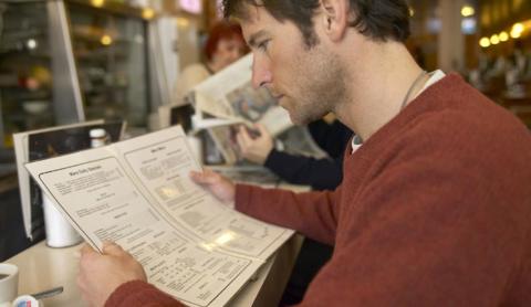 A picture of a man with short brown hair reading a food menu. 