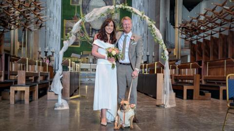 A married couple standing in a church with their dog