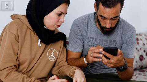 File photo showing a Palestinian couple looking at a mobile phone in Khan Younis, in the south of the Gaza Strip (24 October 2023)