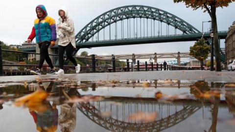 A man and women walk along Newcastle Quayside with the Tyne Bridge in the background