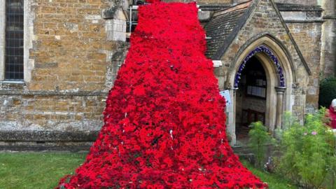 Triangle of poppies, with a narrow point on the church roof widening out as it flows to the ground