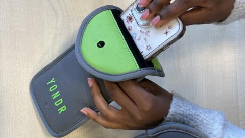 A person removing a phone from a lockable pouch