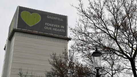File image of Grenfell Tower covered with tarp and a tribute message.