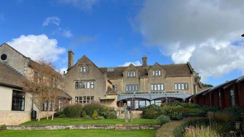 Dorothy House's base in Winsley, from the back showing the garden. It is a large three-storey house with extensions.